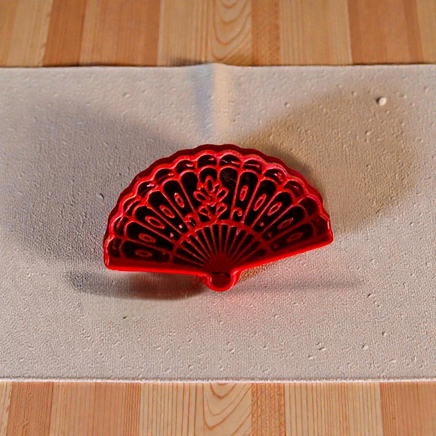 Red floral fan polymer clay cutter on beige textured fabric