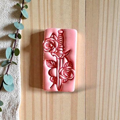 Pink clay impression of dagger with roses beside eucalyptus branch