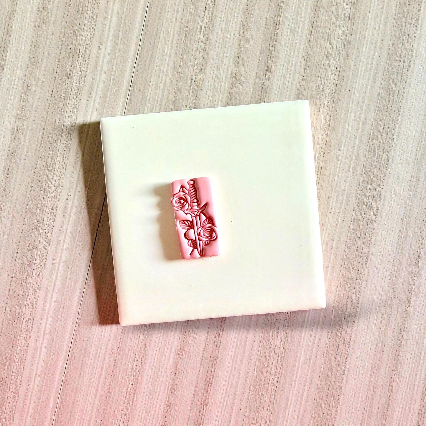 Pink dagger and roses clay impression centered on white tile