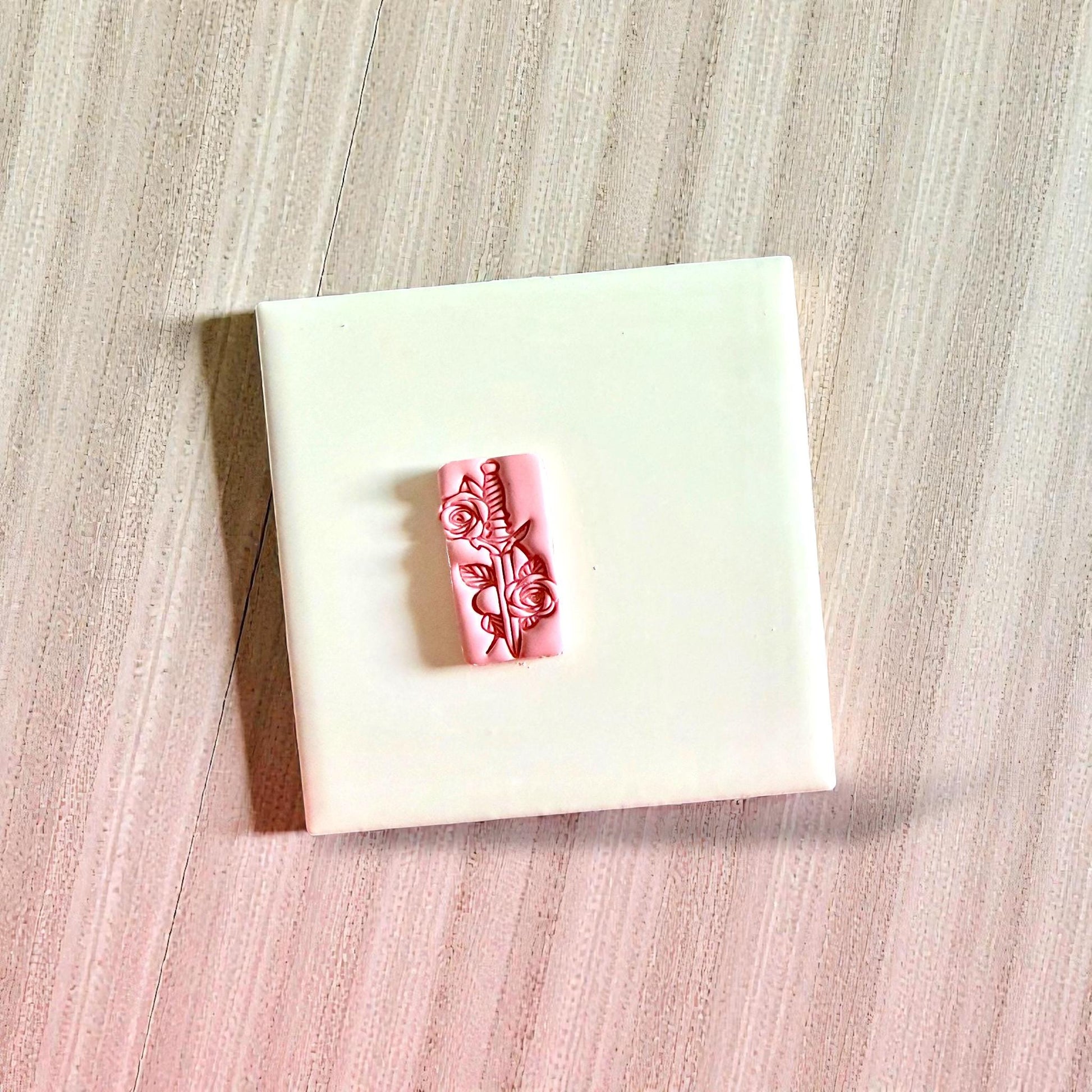 Pink dagger and roses clay impression centered on white tile