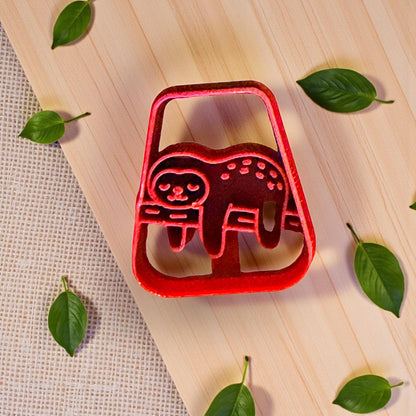Red sloth polymer clay cutter on wood background with scattered green leaves