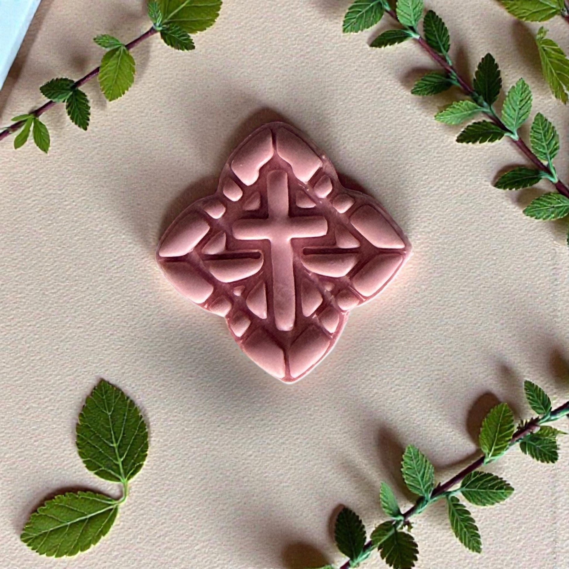 pink cross clay shape surrounded by greenery