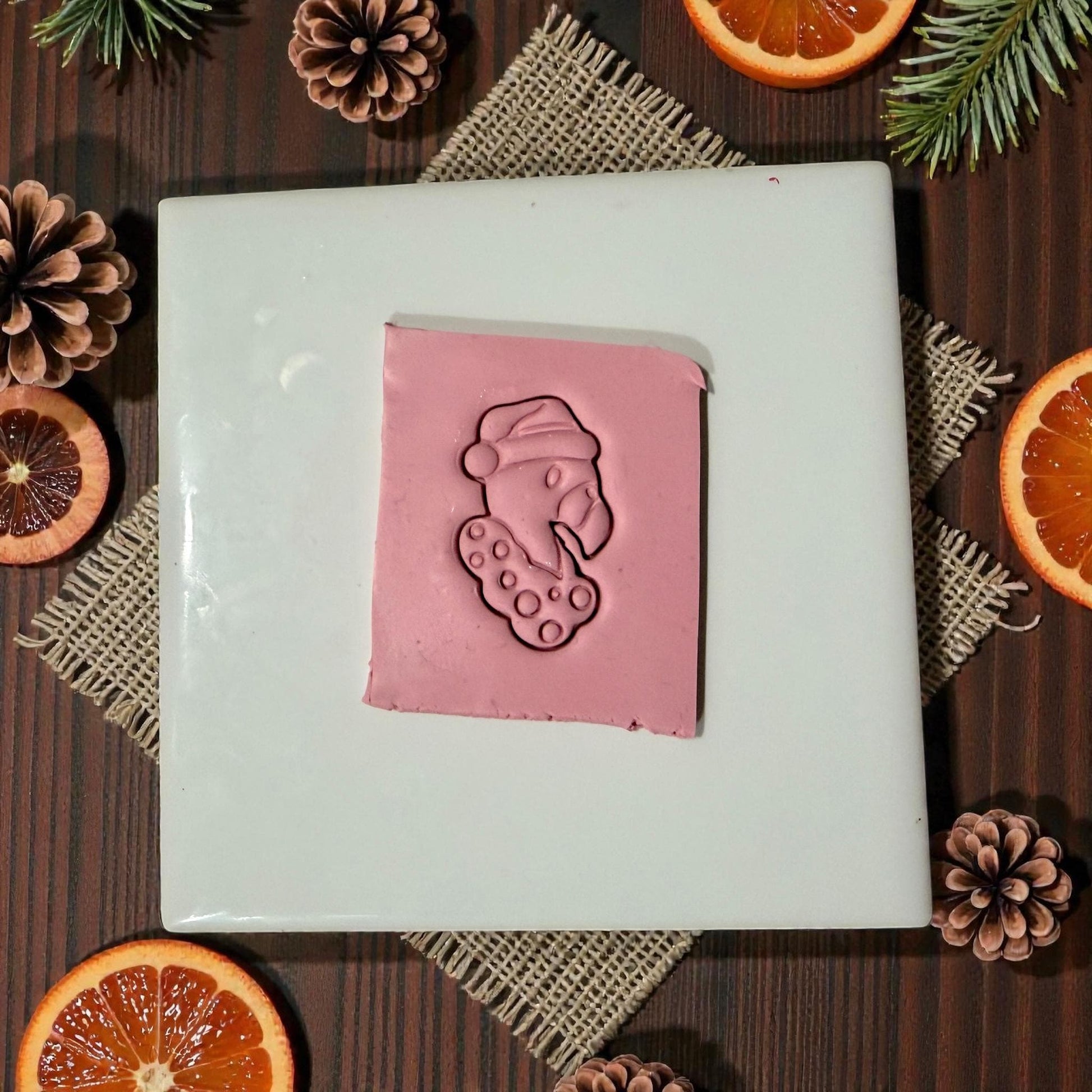 “Pink clay slab with flamingo Christmas imprint surrounded by citrus and pinecones”