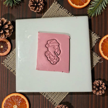 “Pink clay slab with flamingo Christmas imprint surrounded by citrus and pinecones”