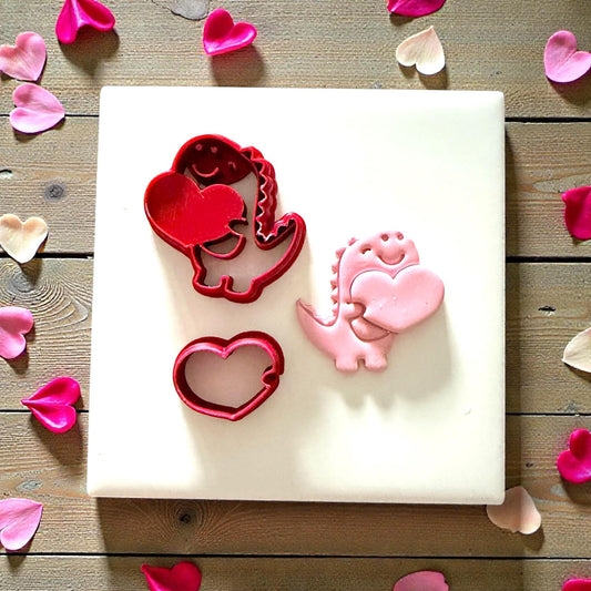 Red dino heart cutter set next to completed pink clay shape