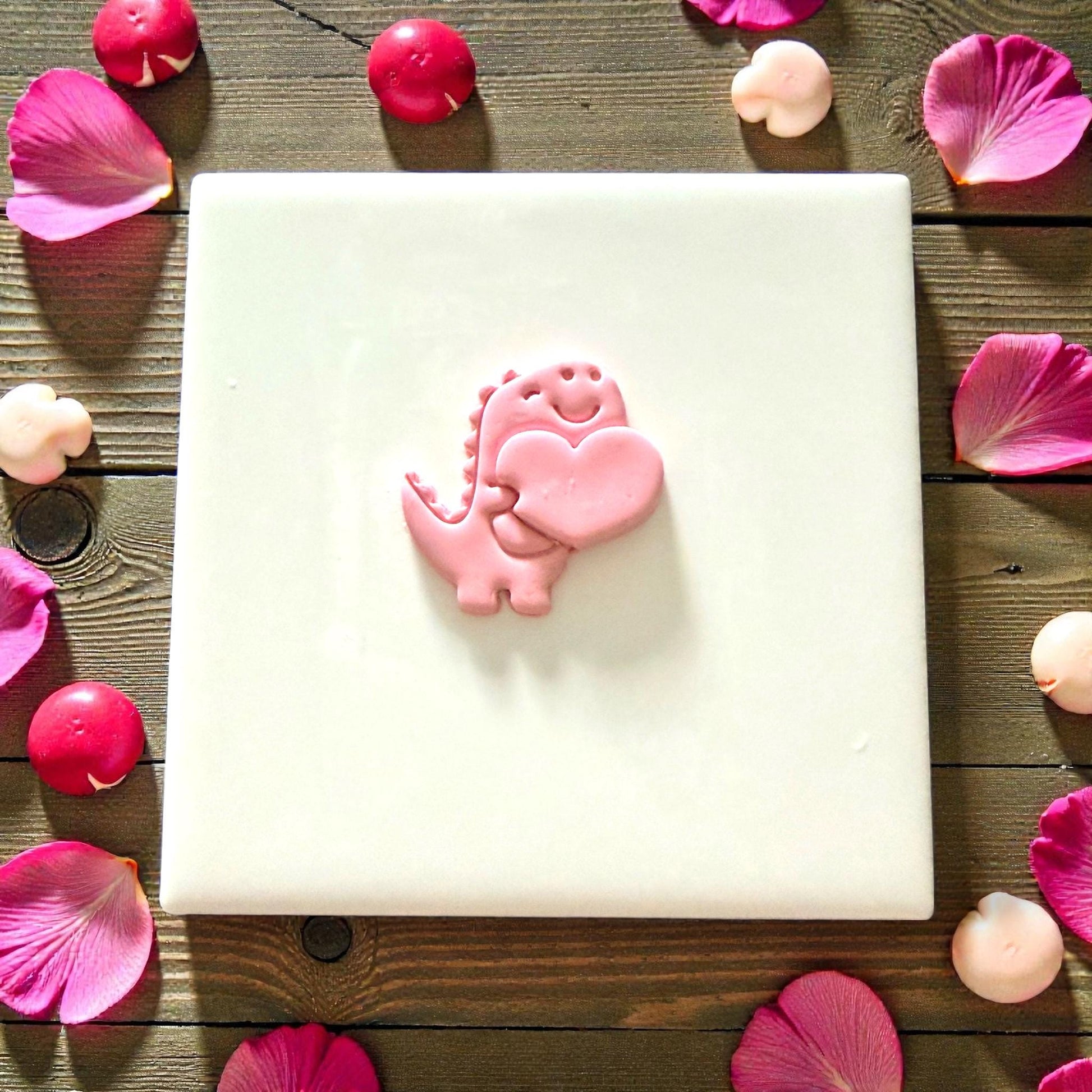 Small pink clay dino heart piece displayed on white tile with petals