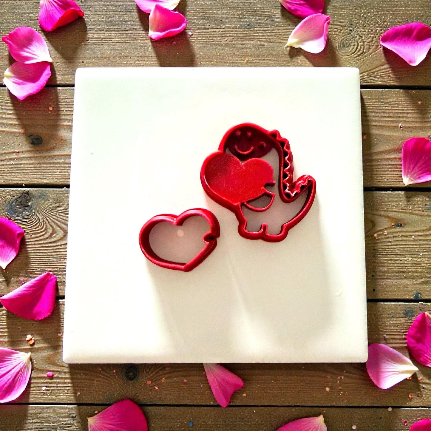 Red polymer clay heart cutter and dino cutter on white tile with petals