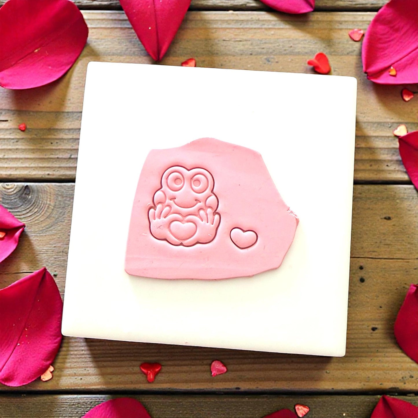 Clay impression of frog holding heart on pink clay slab
