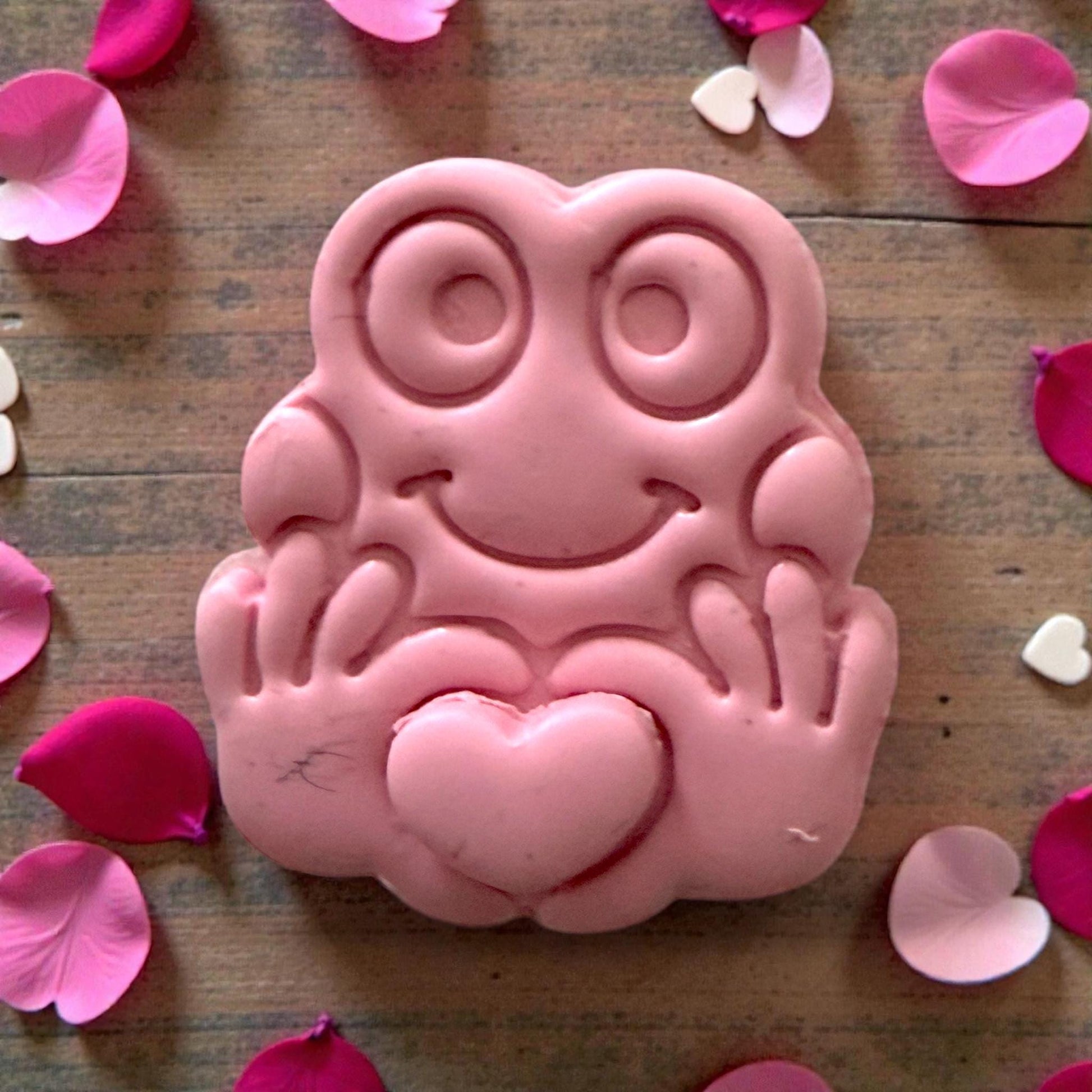 Close-up pink clay frog holding heart with decorative petals