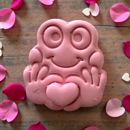 Close-up pink clay frog holding heart with decorative petals
