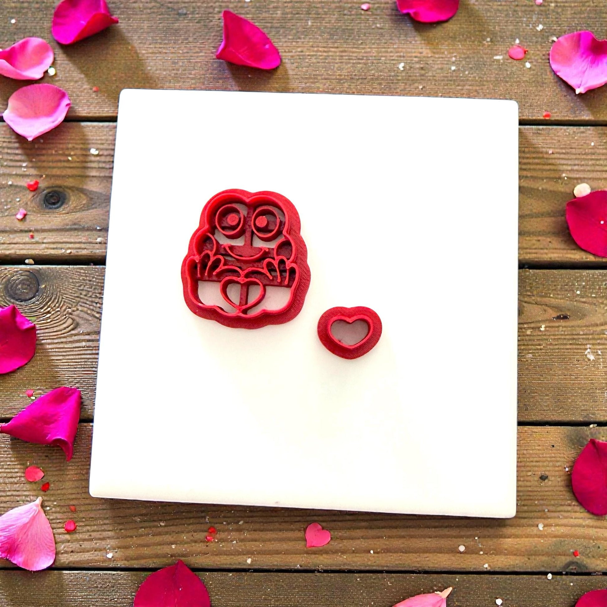 Red frog cutter next to clay frog surrounded by petals