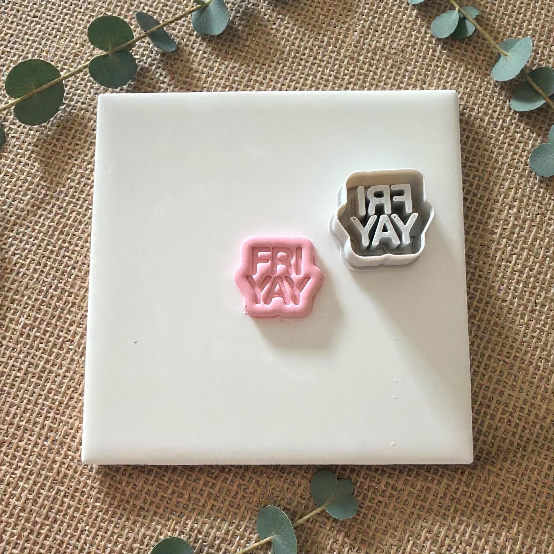 Pink FRIYAY clay shape next to cutter on white tile