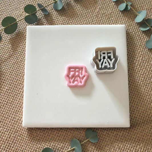 Pink FRIYAY clay shape next to cutter on white tile