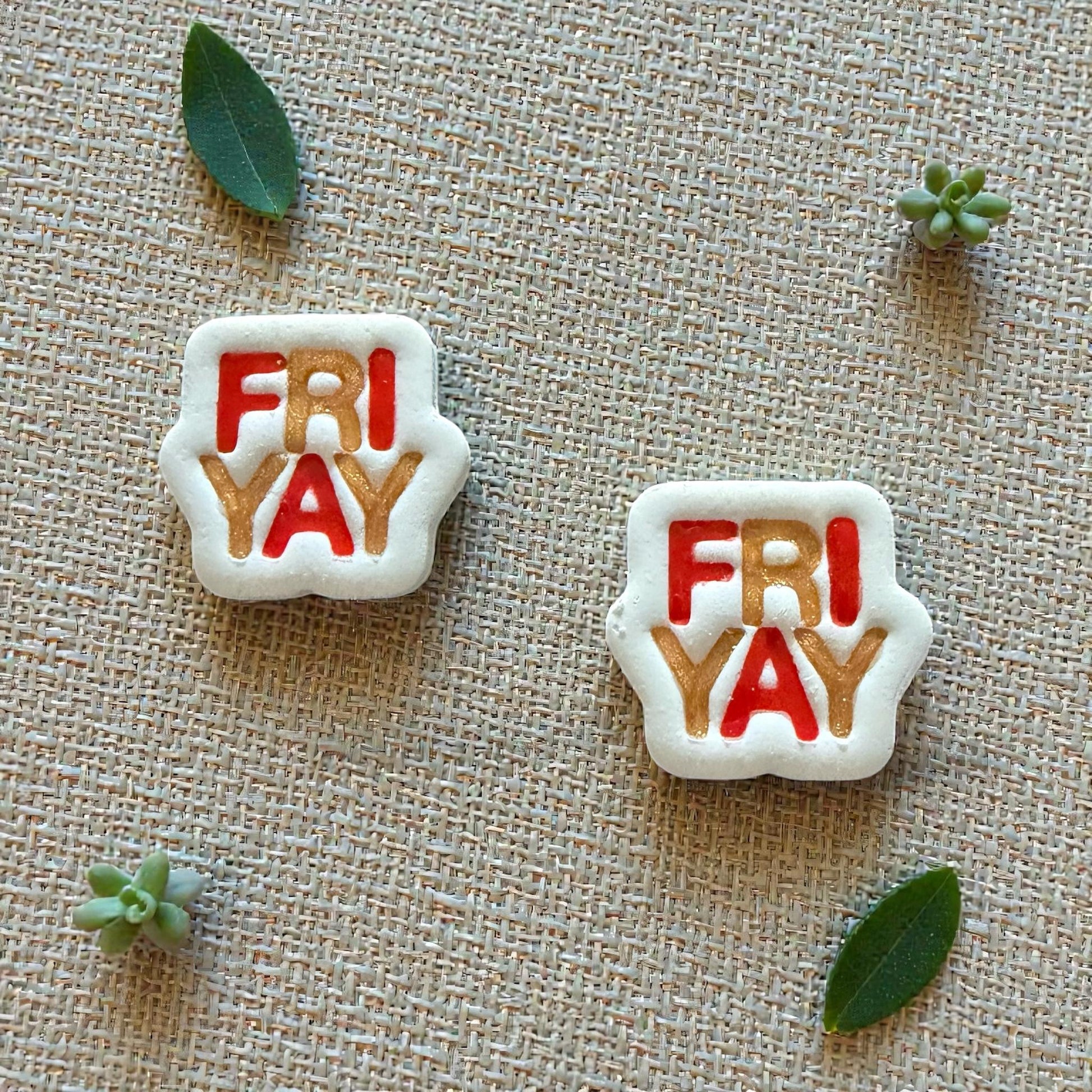 Two FRIYAY clay pieces in red and gold on textured background