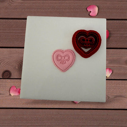 Clay impression of heart bow next to red cutter on white tile