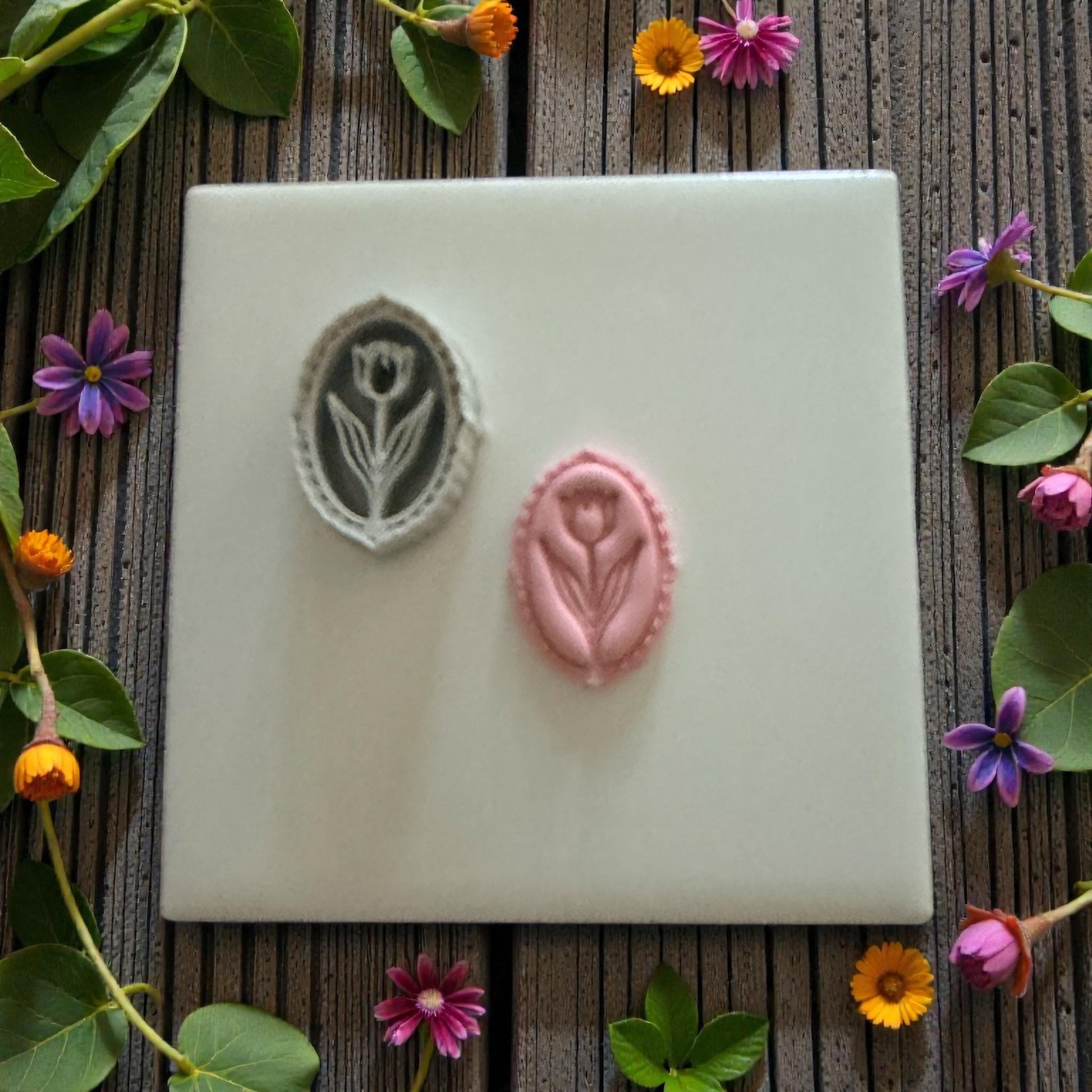 Two tulip clay impressions on a white tile with flowers around