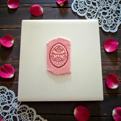 Pink clay with oval lovebird imprint on white tile with rose petals