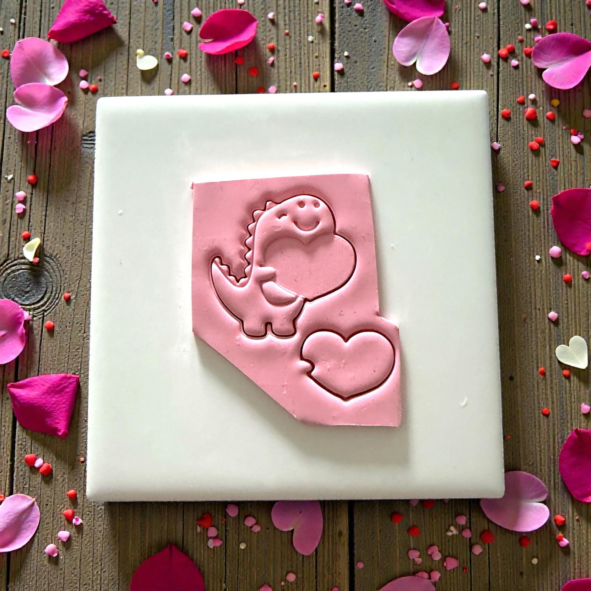 Pink clay impression of dinosaur holding a heart surrounded by rose petals
