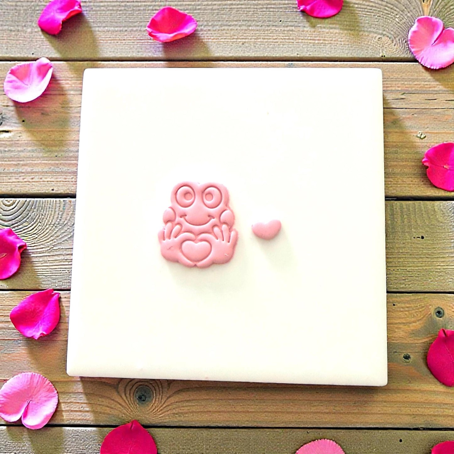 Small pink clay frog with heart resting on white tile