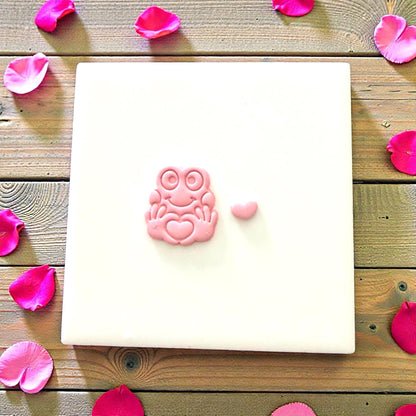 Small pink clay frog with heart resting on white tile
