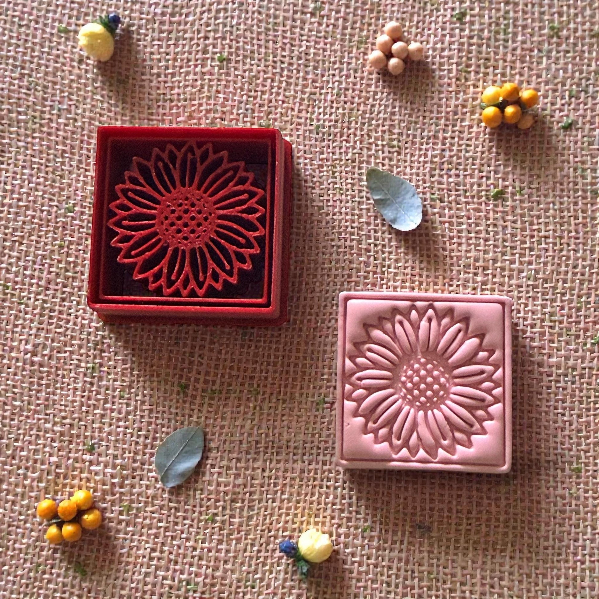 sunflower clay cutter and stamped clay surrounded by small decorative leaves