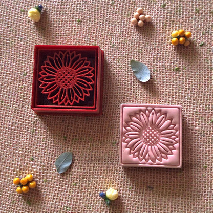 sunflower clay cutter and stamped clay surrounded by small decorative leaves