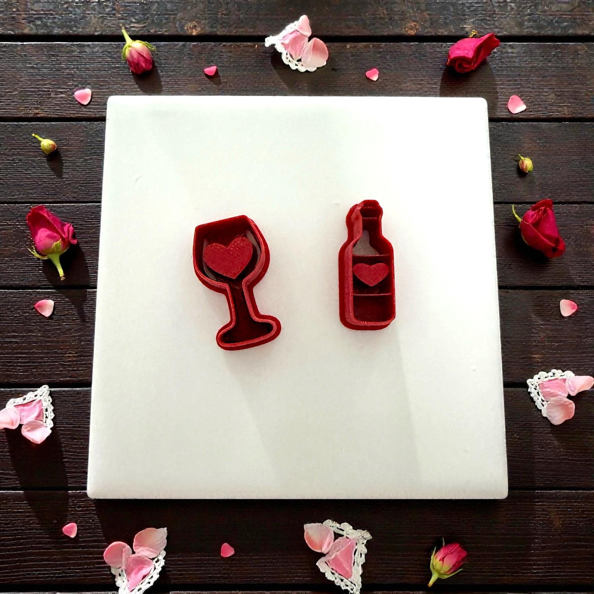 Two wine clay cutters displayed on white tile with scattered petals
