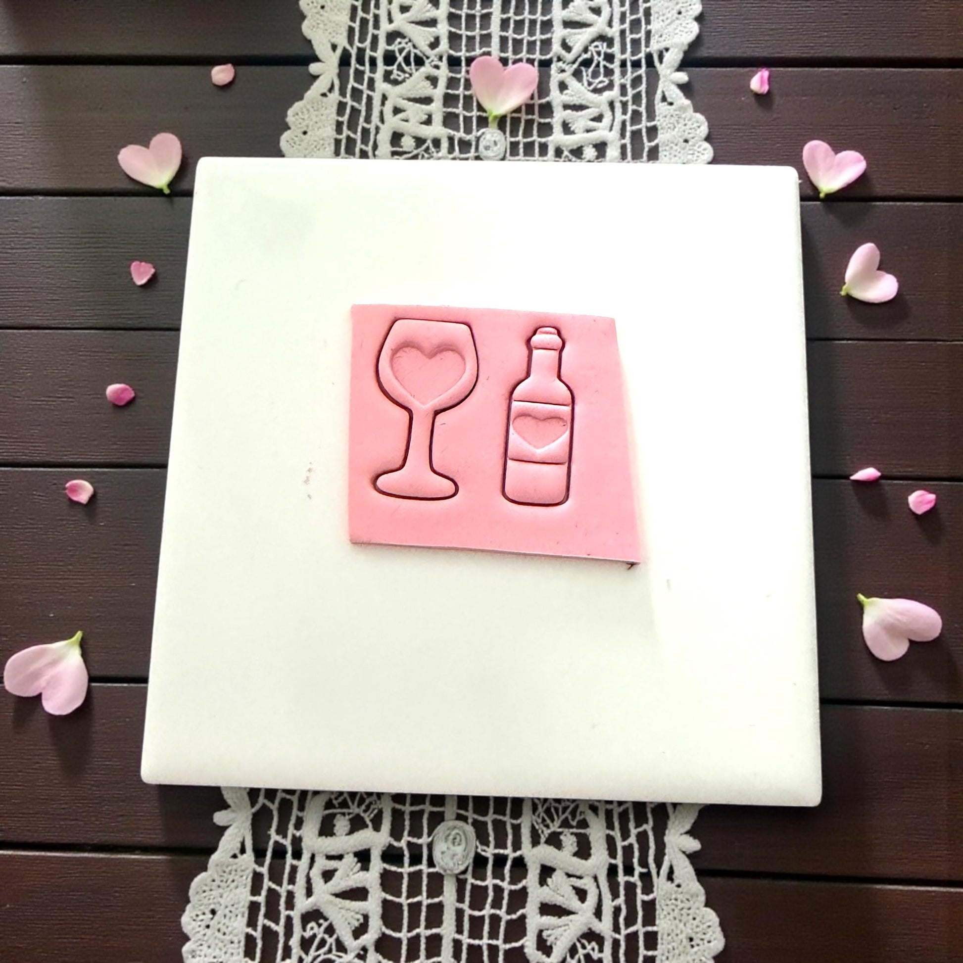 Pink clay wine glass and bottle with heart cutouts surrounded by petals
