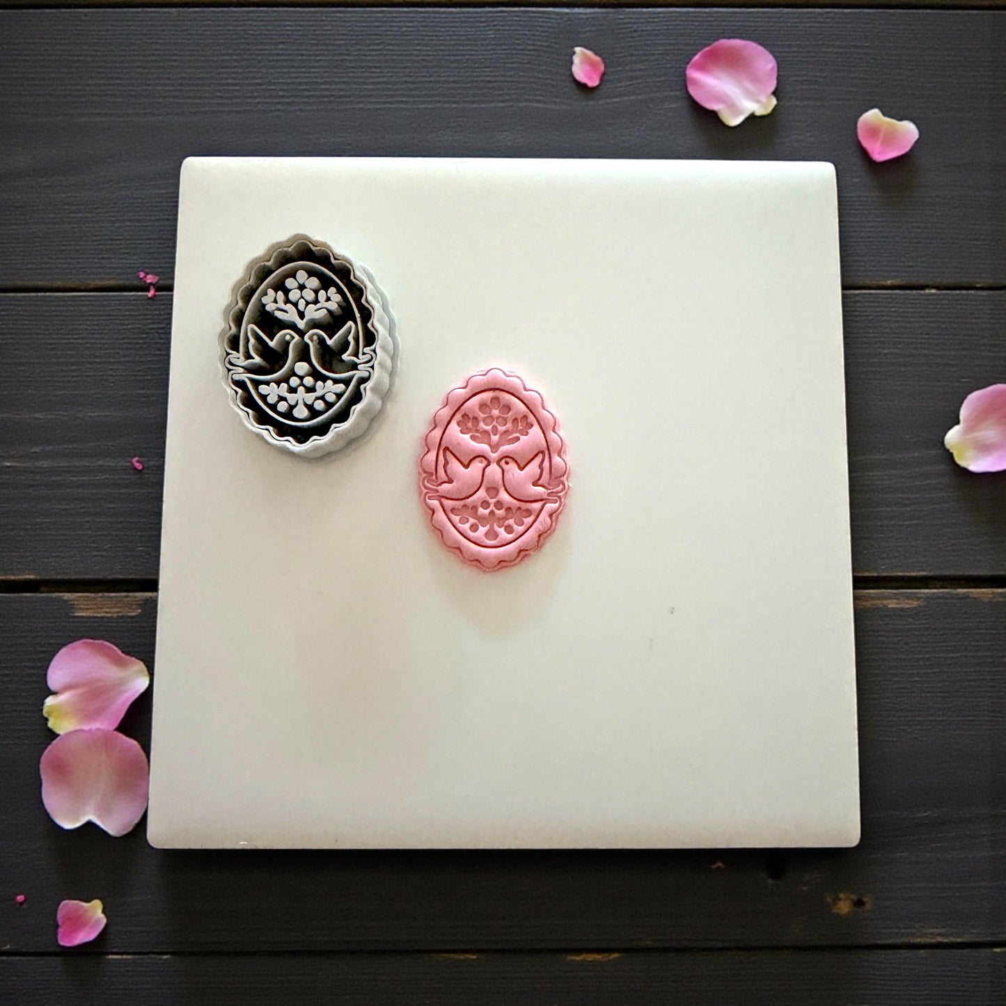 Gray cutter and pink clay imprint of lovebirds displayed on tile
