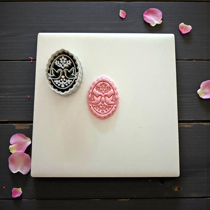 Gray cutter and pink clay imprint of lovebirds displayed on tile