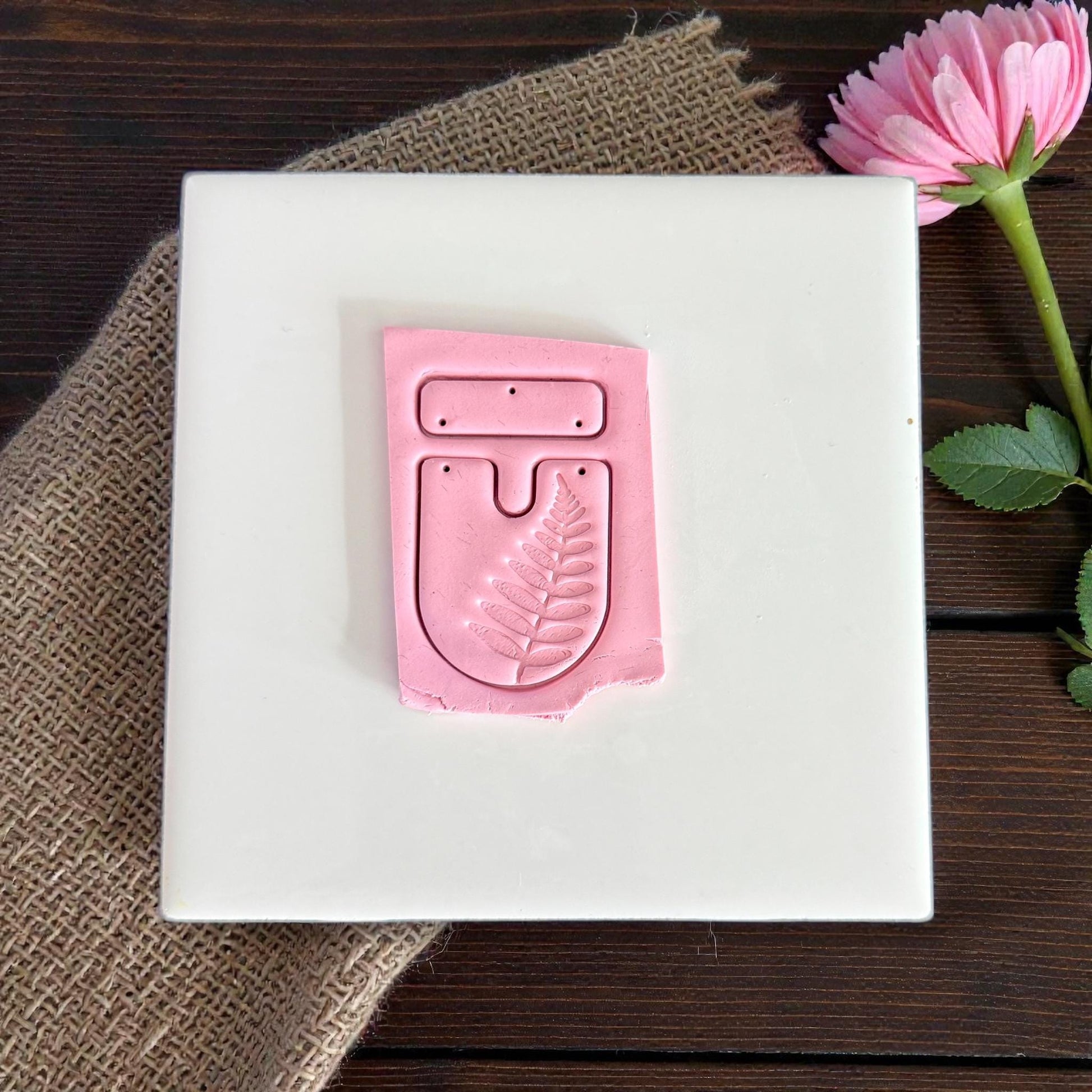 Pink clay impression of fern U-shape cutter and bar on white tile