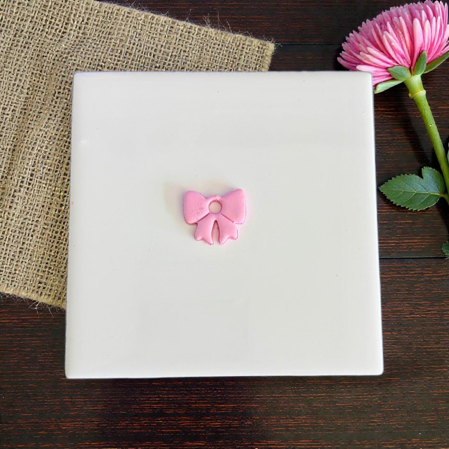Small pink bow clay charm centered on white board