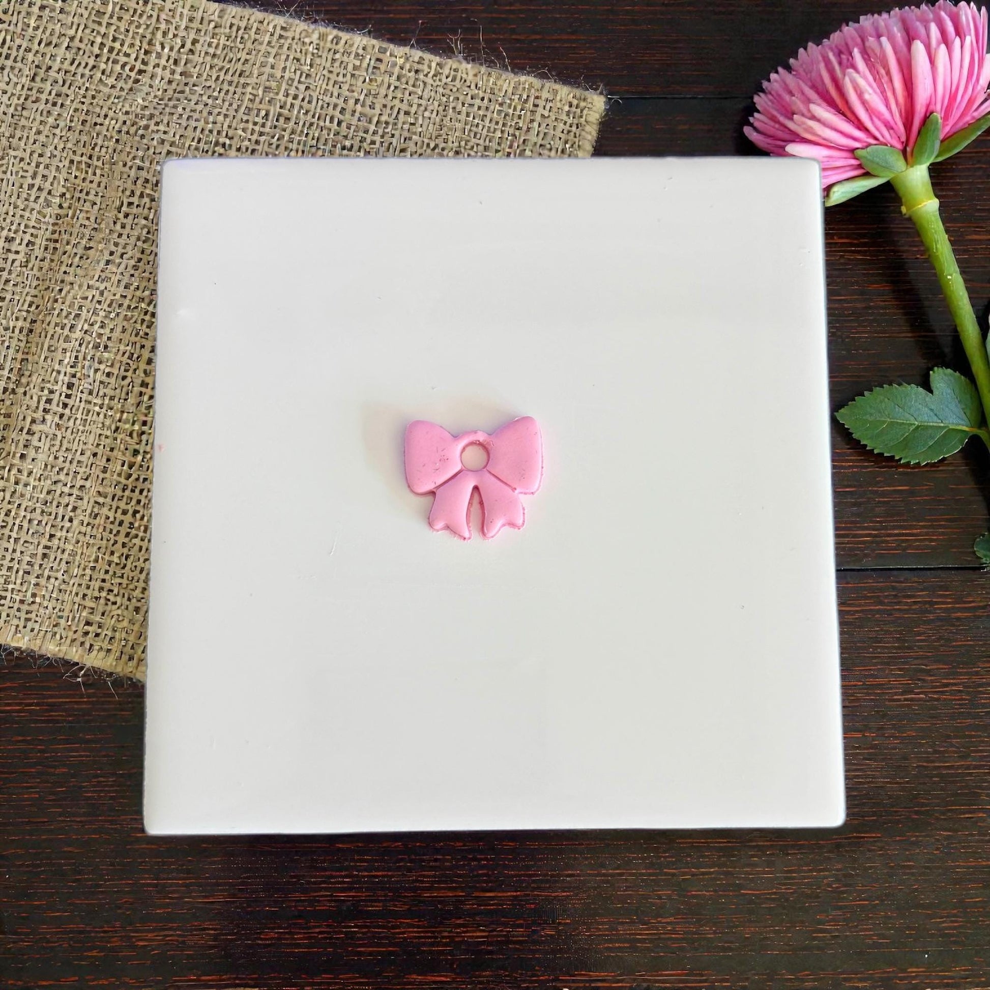 Small pink bow clay charm centered on white board