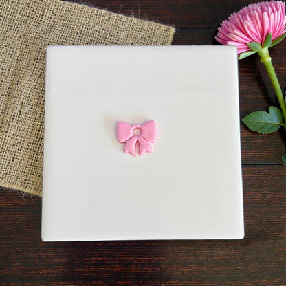 Small pink bow clay charm centered on white board
