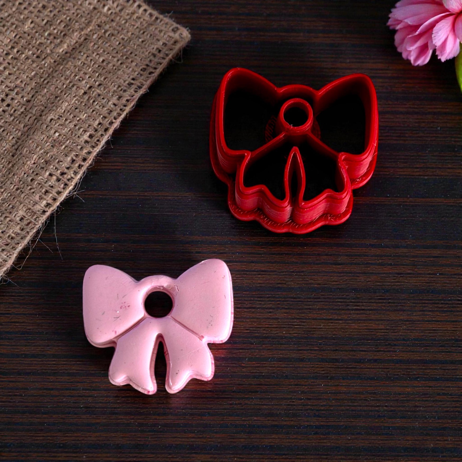Pink bow charm next to red bow cutter on dark wood surface
