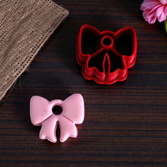 Pink bow charm next to red bow cutter on dark wood surface