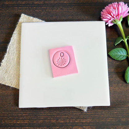 Pink clay imprint showing round sun swirl charm design