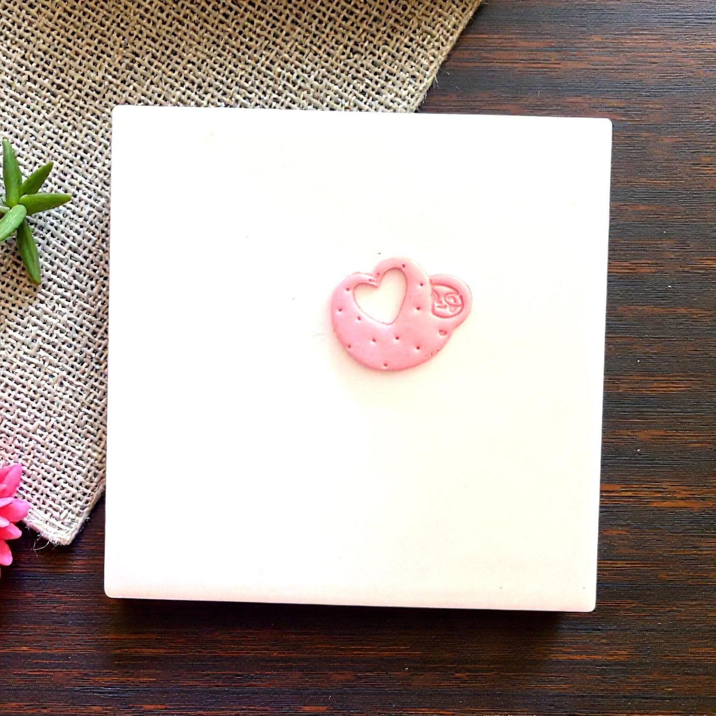 Small pink sloth heart clay piece centered on tile
