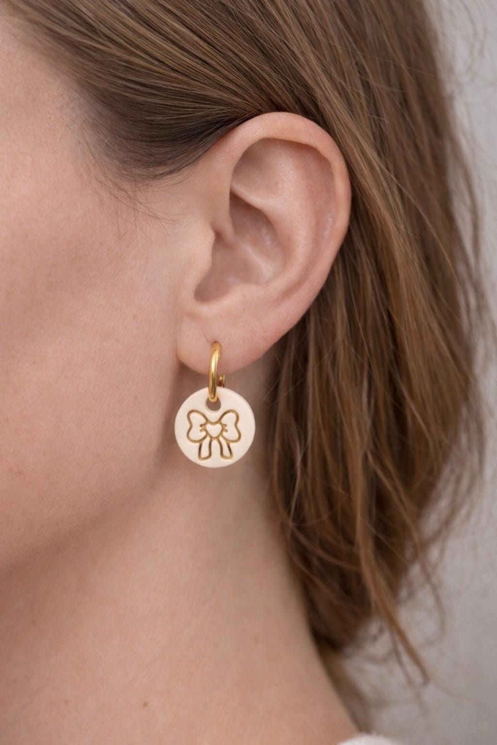 girl wearing beige round heart bow huggies earrings