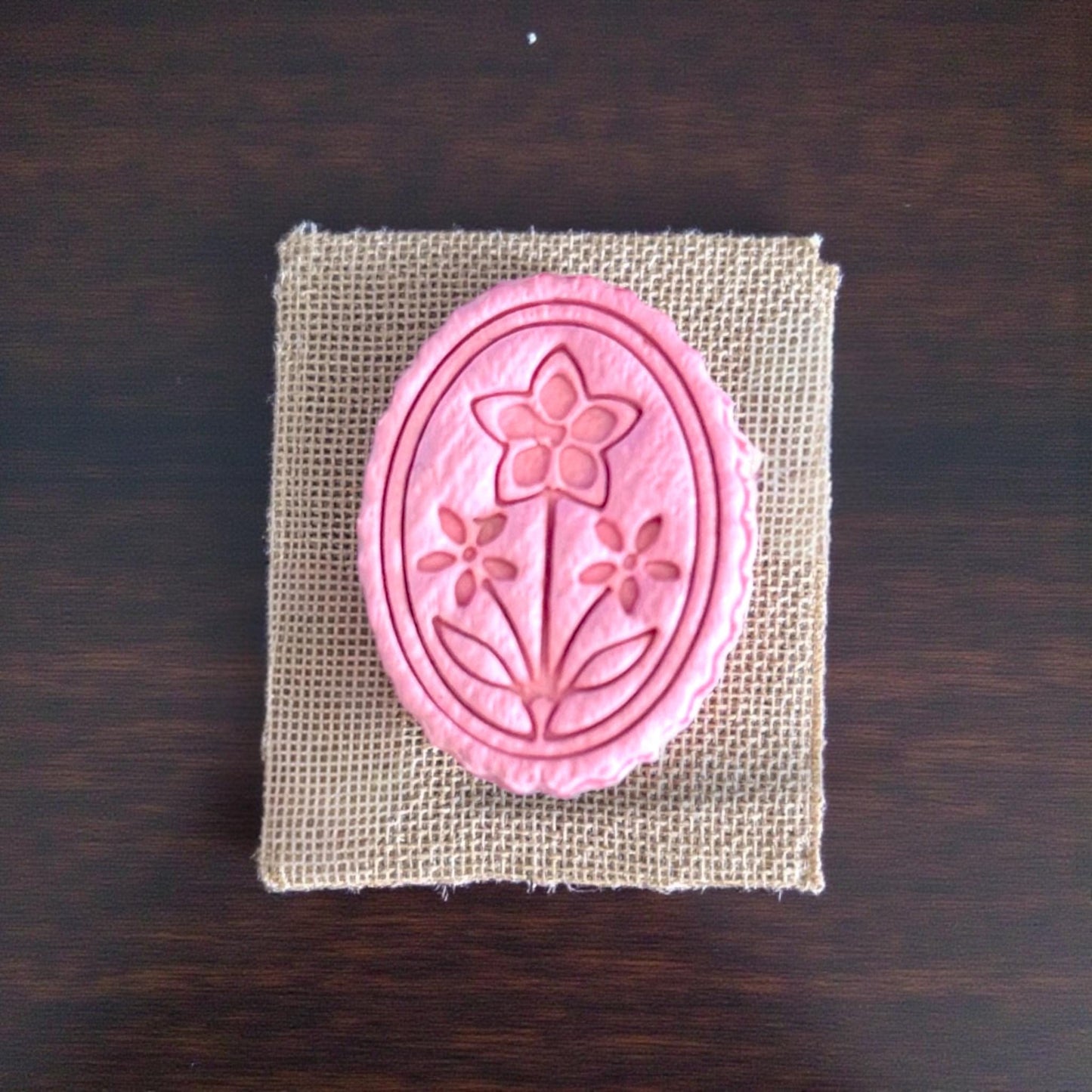 small floral cameo clay cutout displayed on burlap