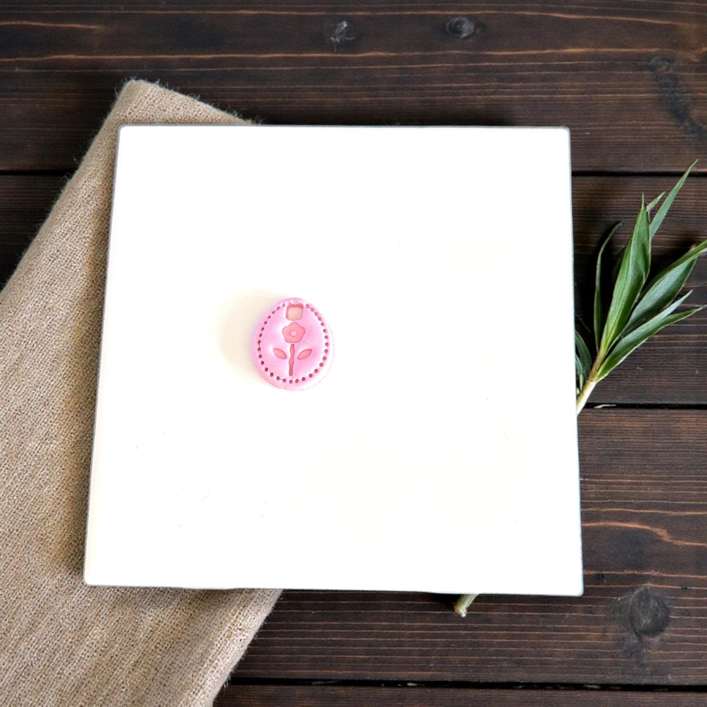tiny oval flower clay charm displayed on white tile