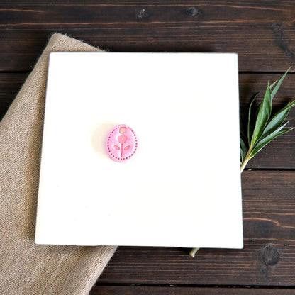 tiny oval flower clay charm displayed on white tile