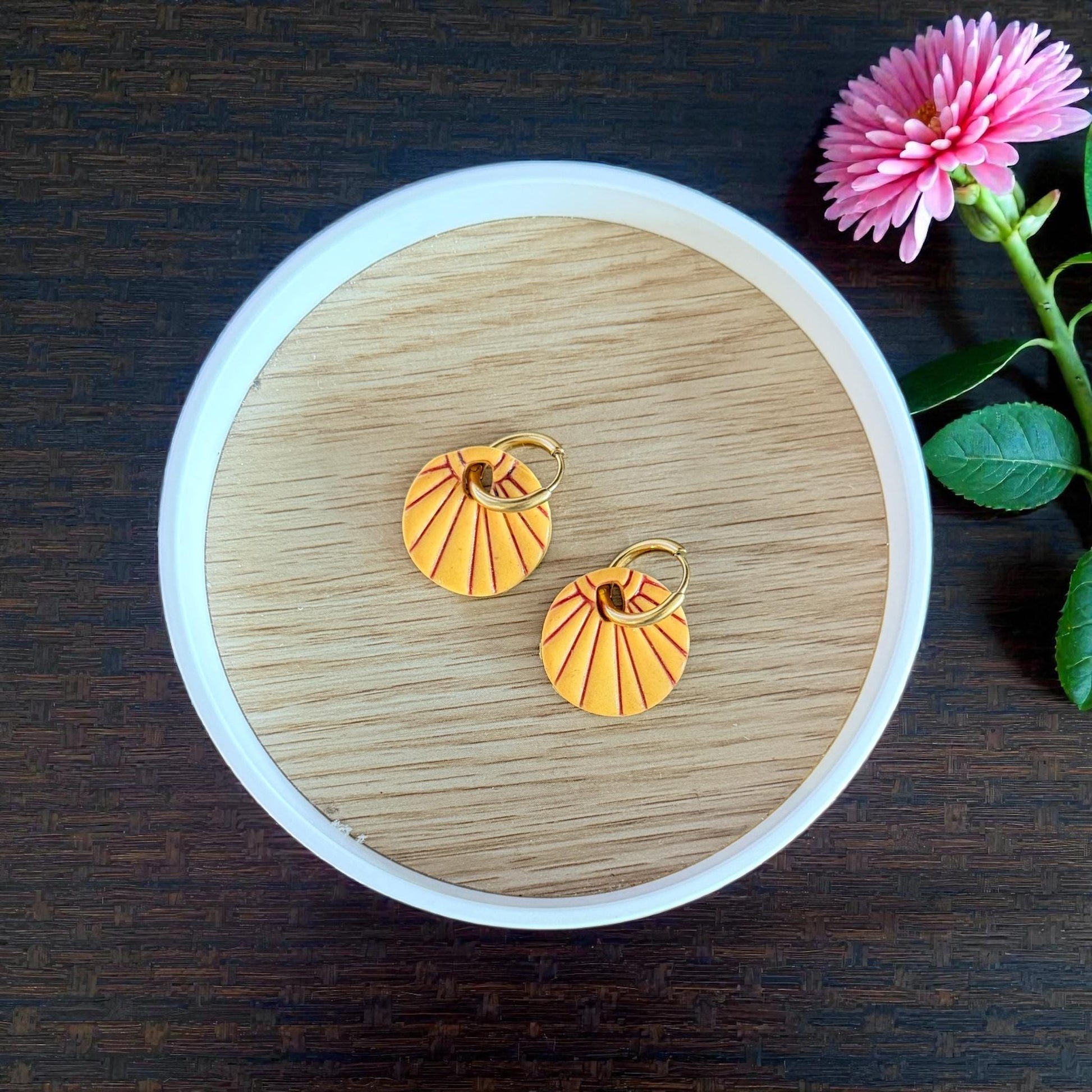 Orange sunburst charms with gold hoops in round dish
