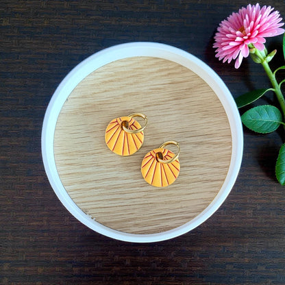 Orange sunburst charms with gold hoops in round dish