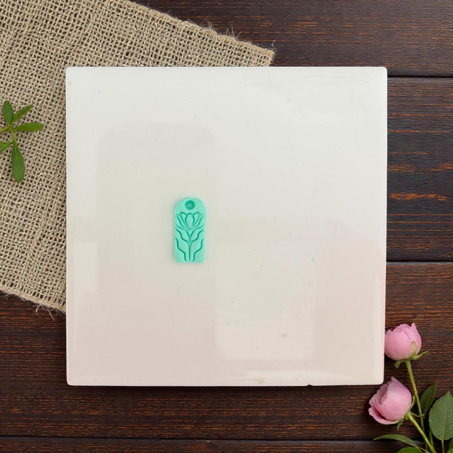 Small floral clay charm centered on white tile