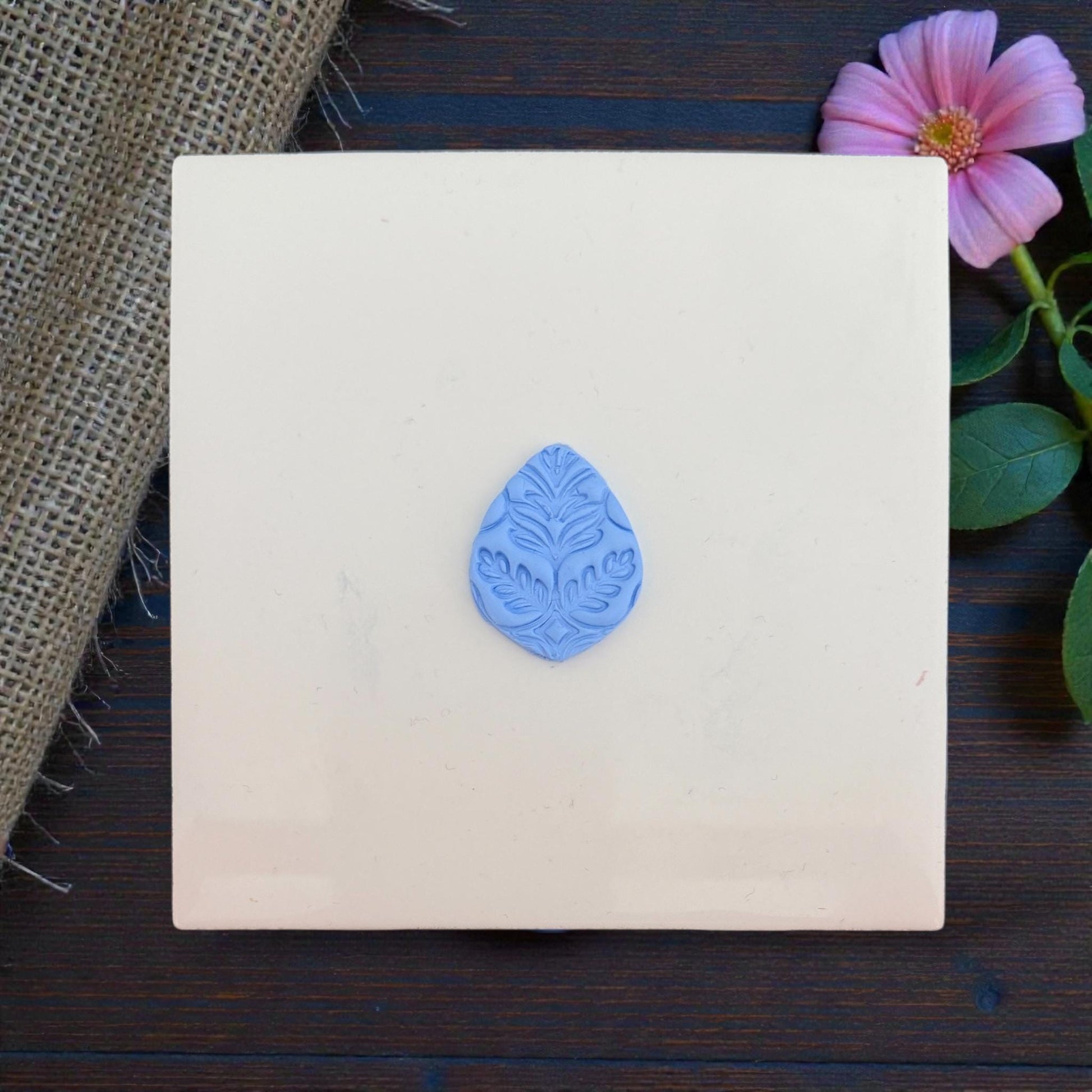 Centered botanical clay imprint displayed on square ceramic tile