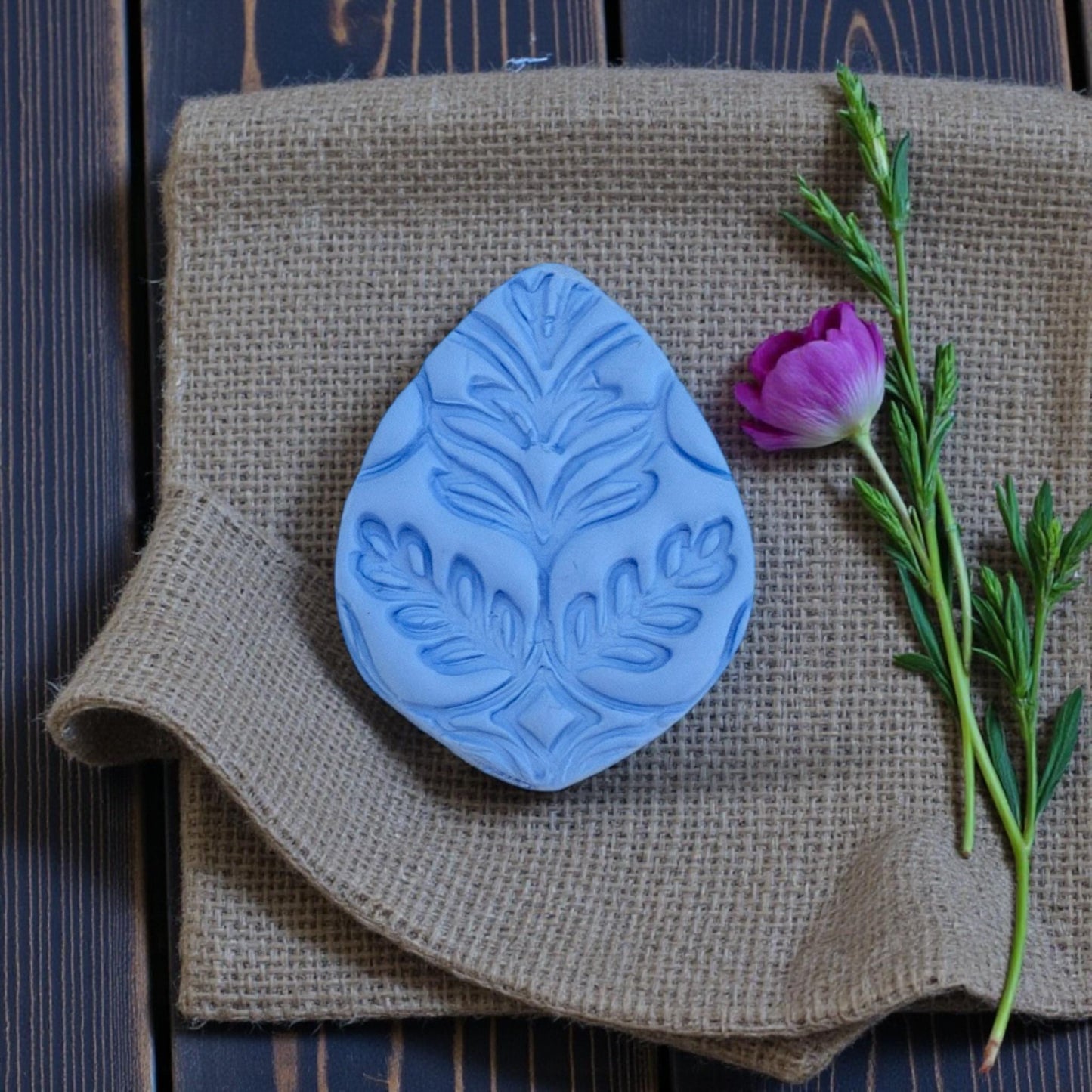 Blue clay imprint with botanical leaf pattern on burlap fabric