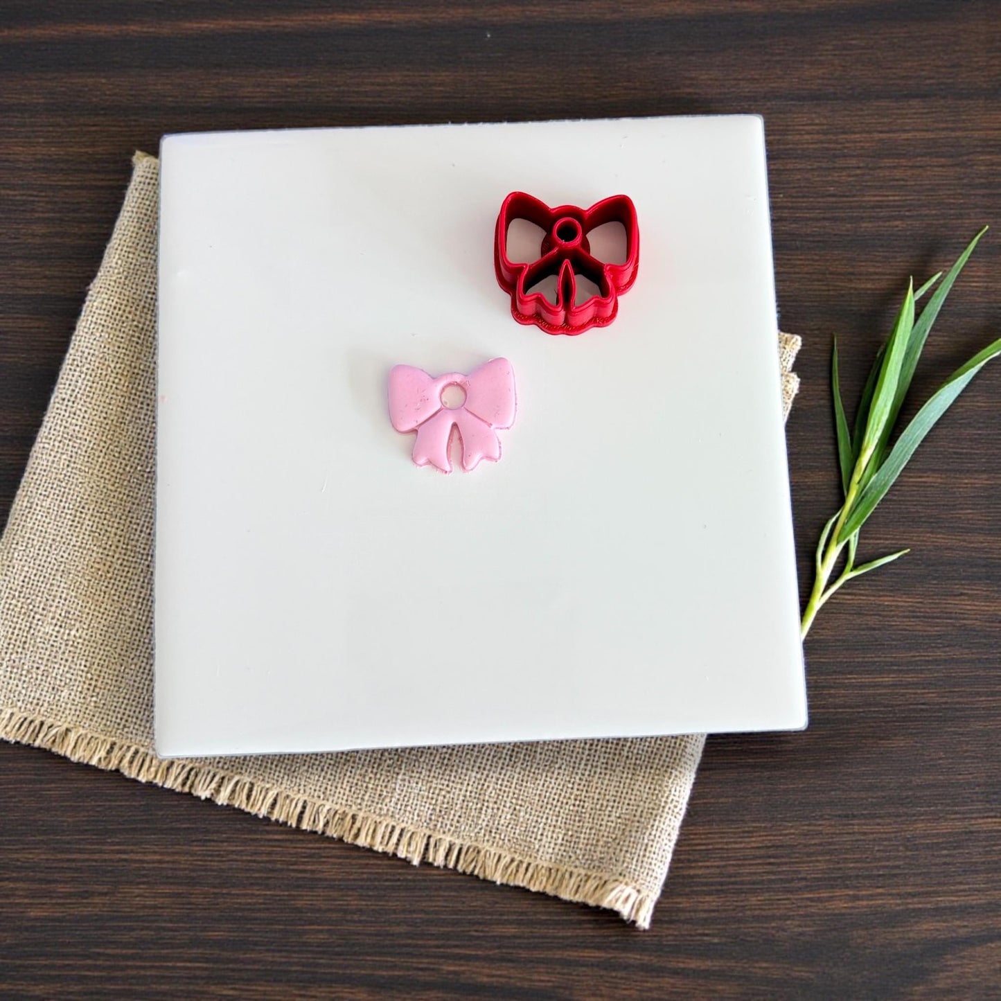 Pink bow charm and red bow cutter displayed on white tile