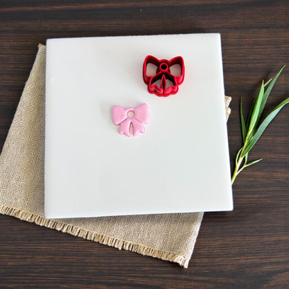 Pink bow charm and red bow cutter displayed on white tile