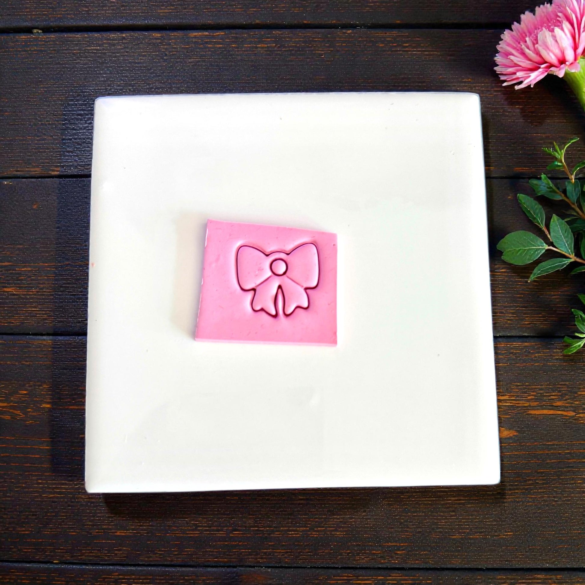 Pink clay slab with bow charm impression on white background